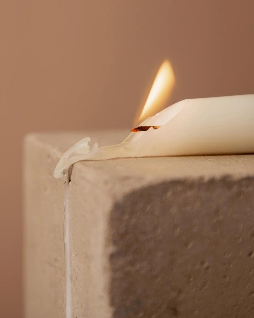 A white candle on its side, burning and dripping wax over the edge of a brick