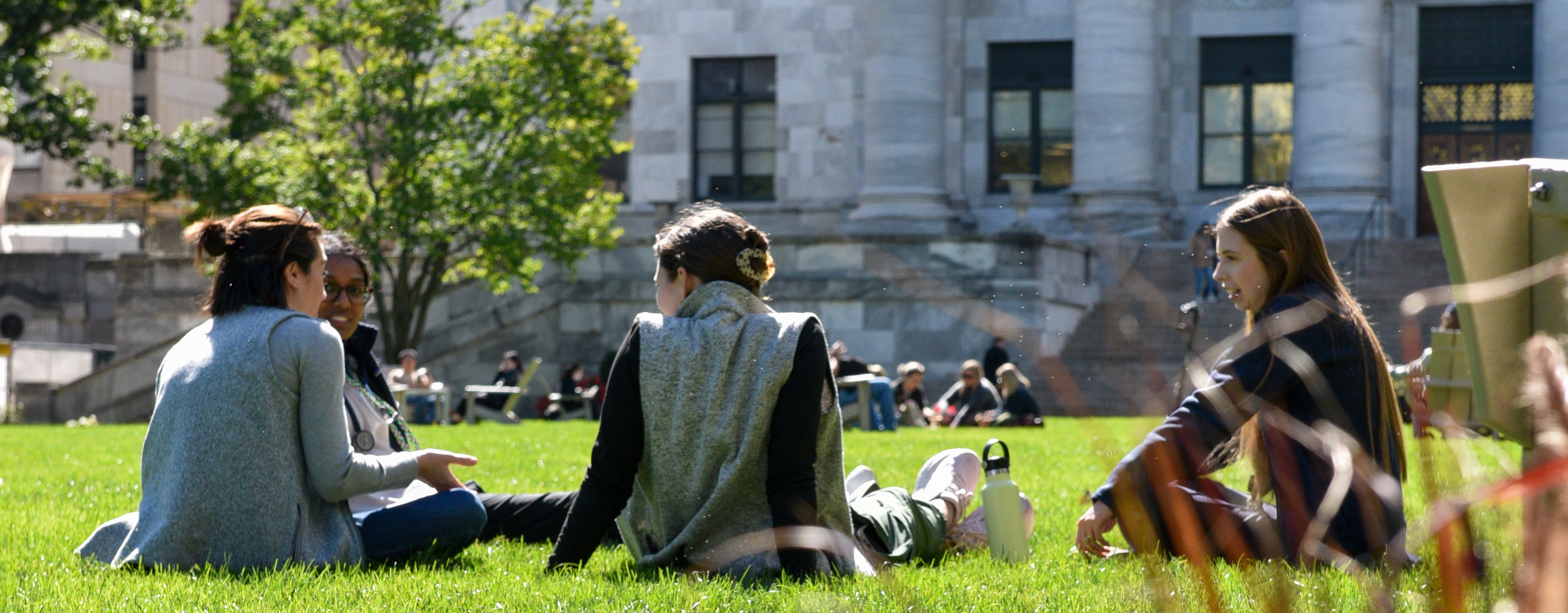 Three students sitting on the HMS Quad lawn chatting.