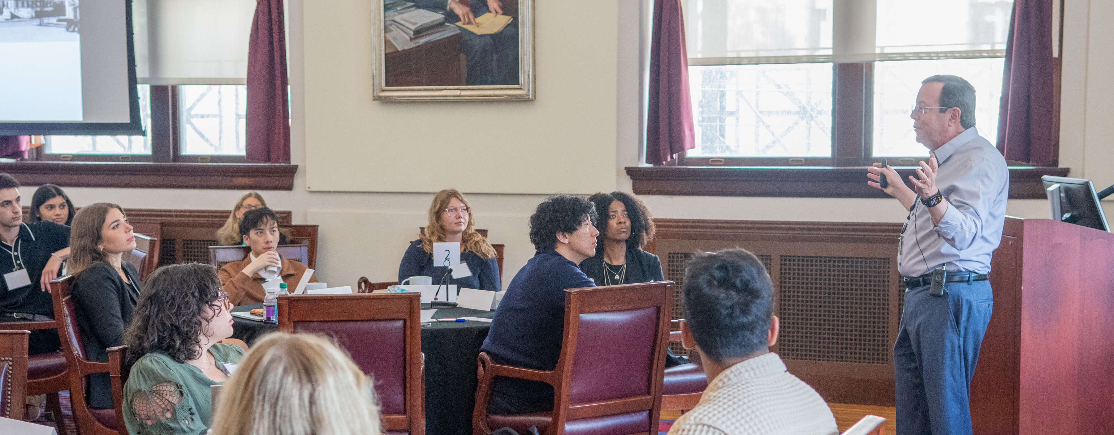 Students seated at tables watch a presenter.