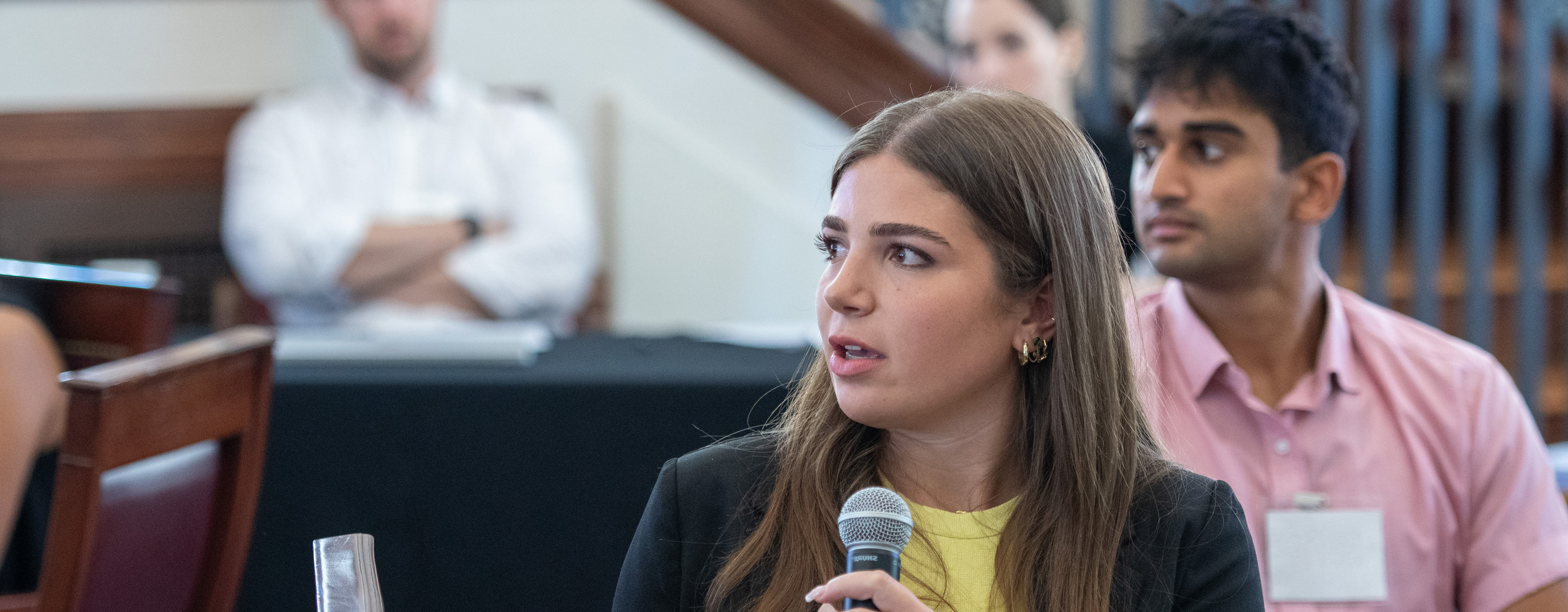 Student with long hair speaking into microphone while seated.