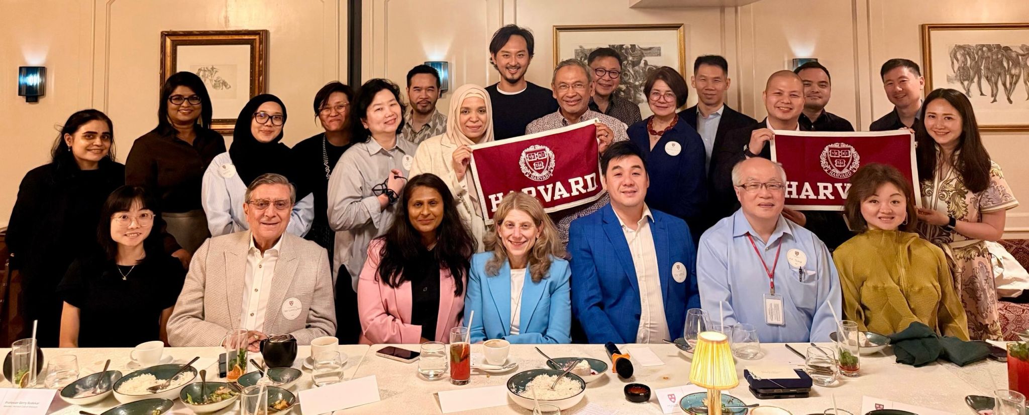 Center alumni and colleagues gathered at dinner holding Harvard banners.