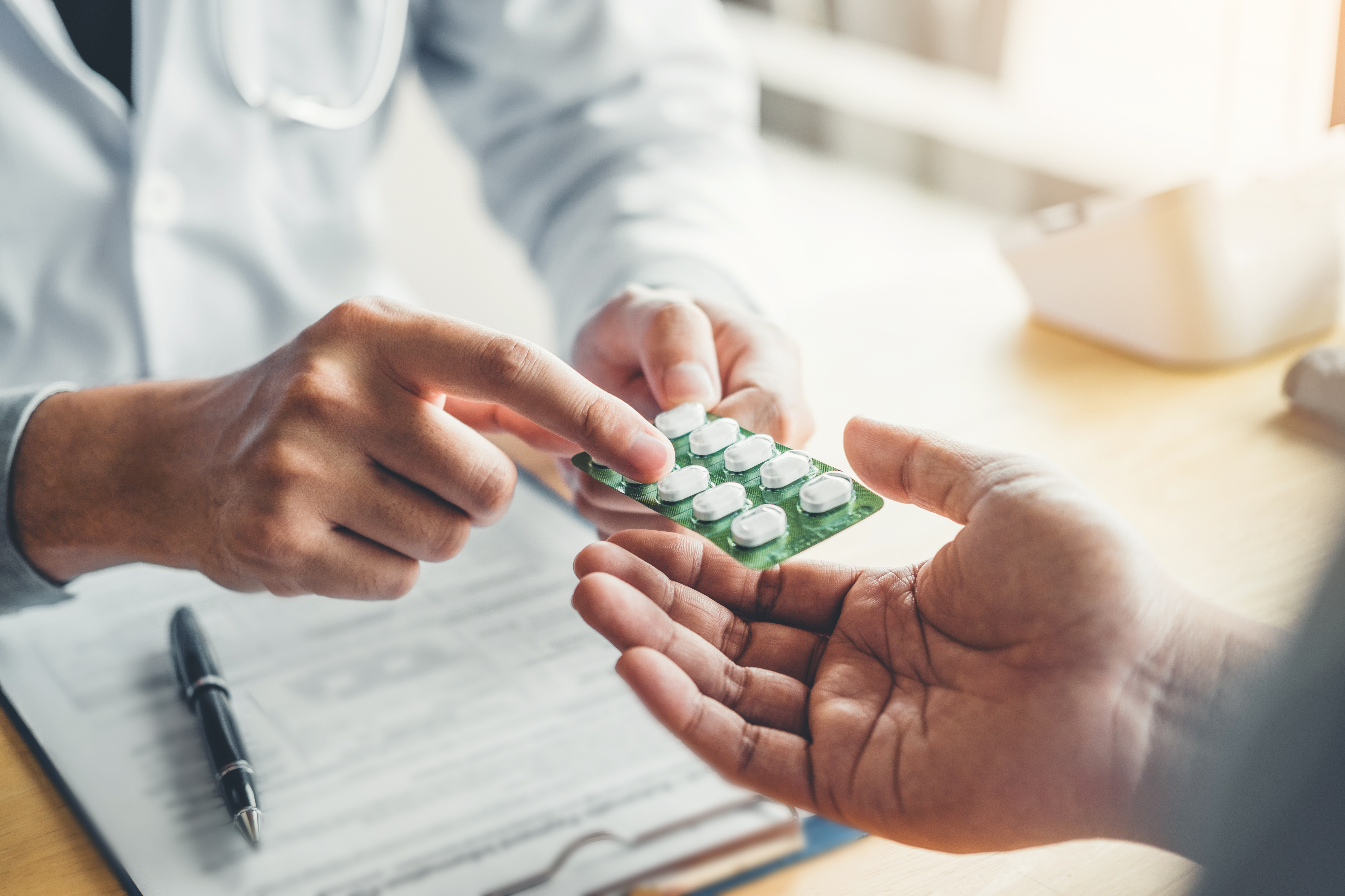 A physician handing pills in a blister pack to a patient.