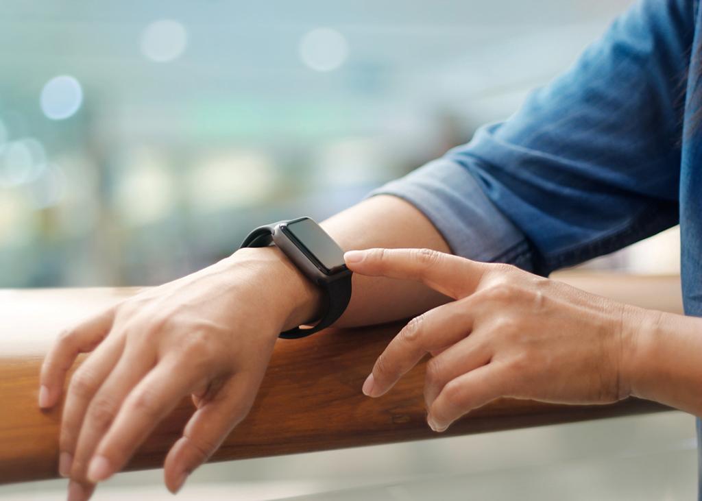 Closeup of a person's hand pointing to a black smartwatch on their other wrist