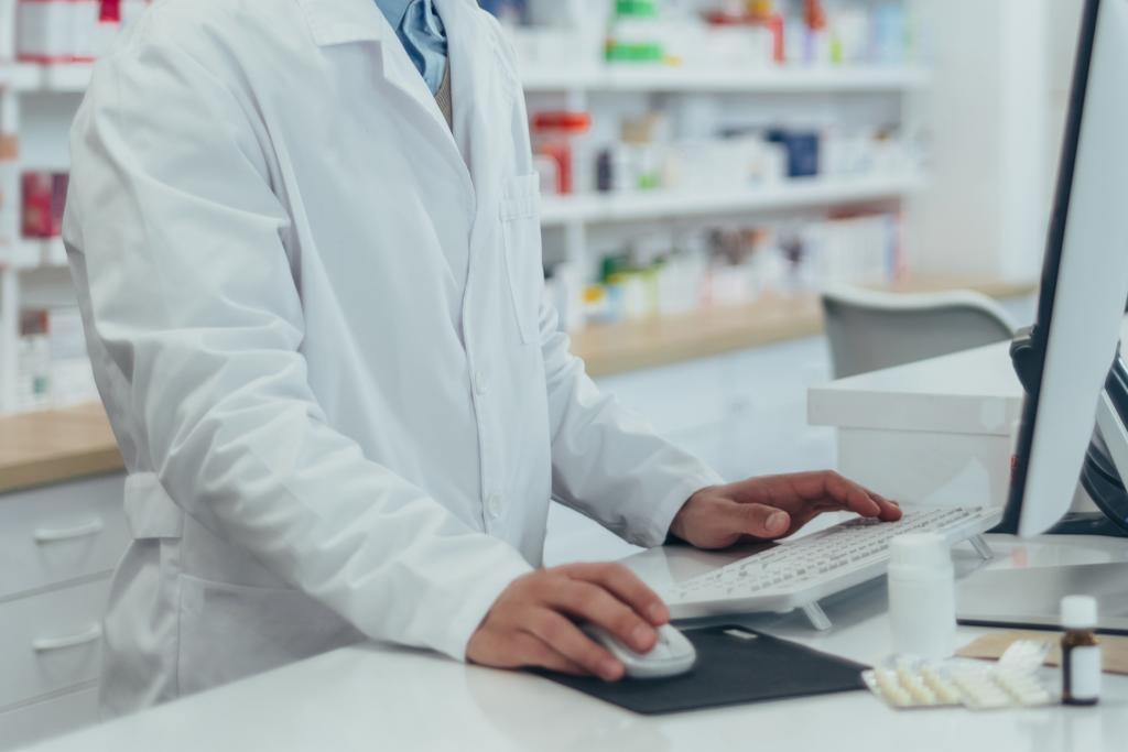 Closeup of pharmacist using a computer with shelves of medicine behind them