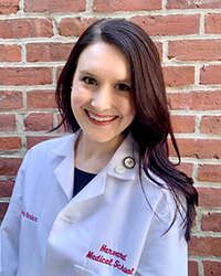 Mary Barber smiling, wearing a white lab coat with her name and Harvard Medical School written in crimson red font