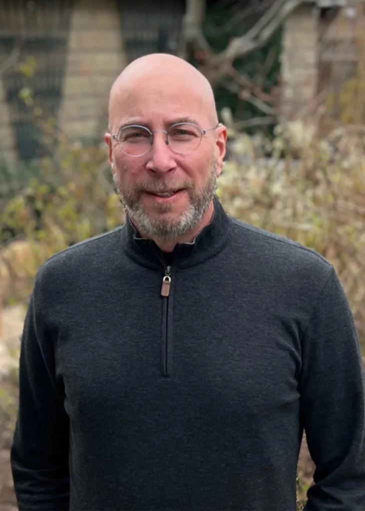 Jay Baruch standing outside wearing glasses and a zipped-up sweater