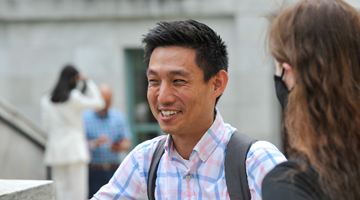 Student smiling, wearing a blue plaid shirt and black backpack